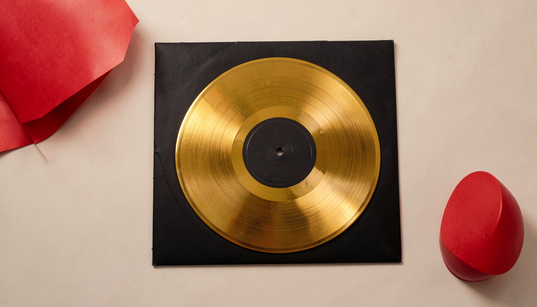Close-up overhead of a golden vinyl record resting on its sleeve, warm amber and black tones, rich and tactile