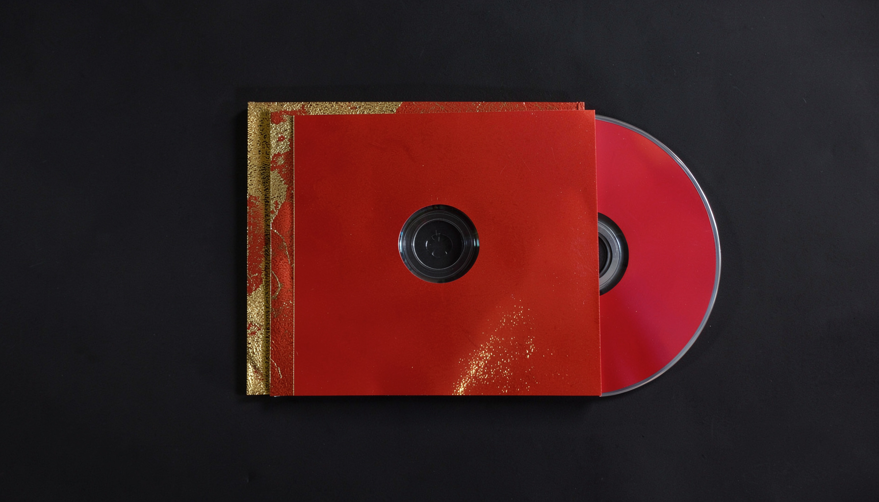 Overhead flat-lay of a CD digipack with gold foil print accents, dark background with subtle reflections