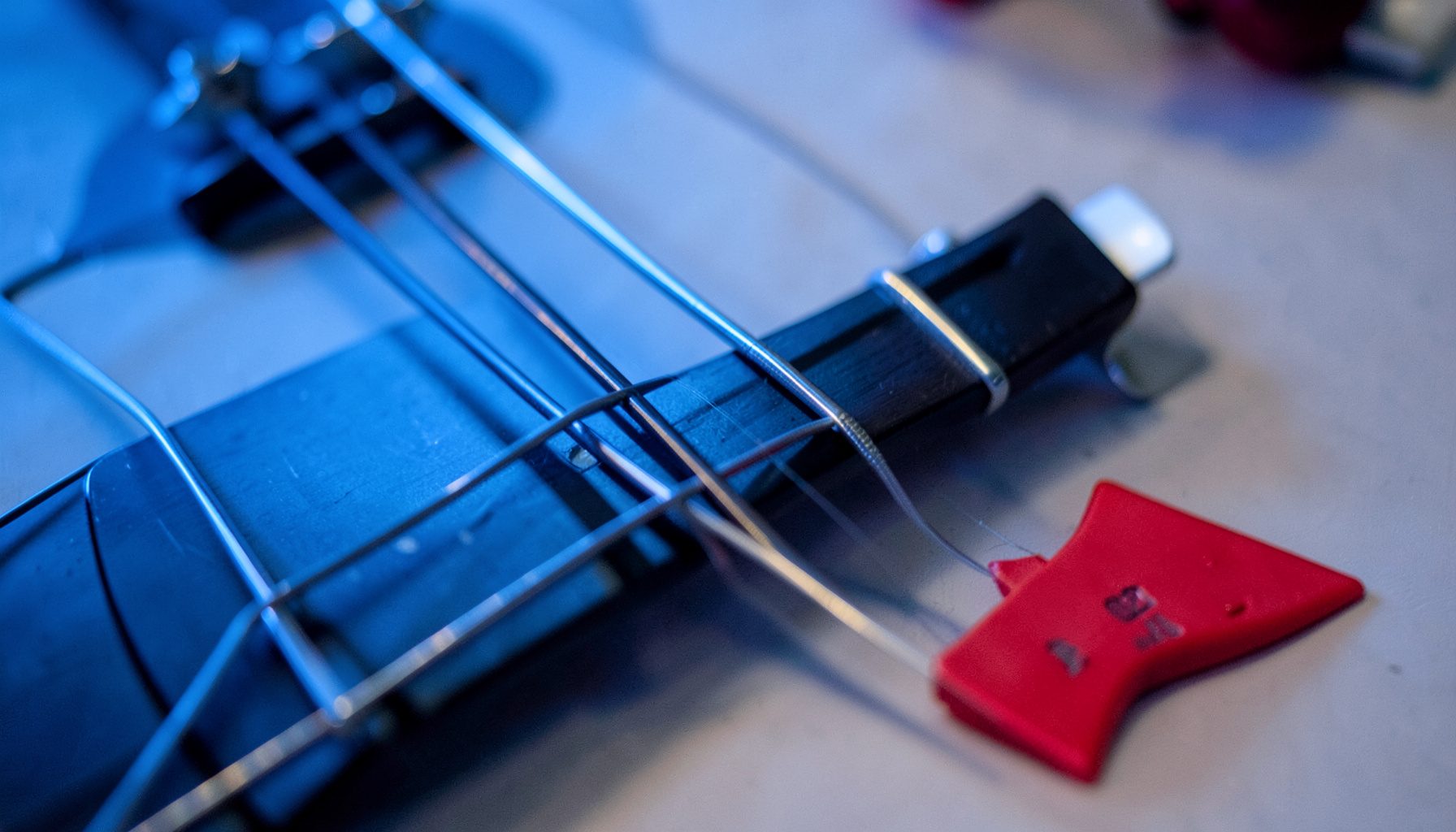 Close-up of guitar strings and fretboard under cool blue stage light, shallow depth of field with bokeh effects