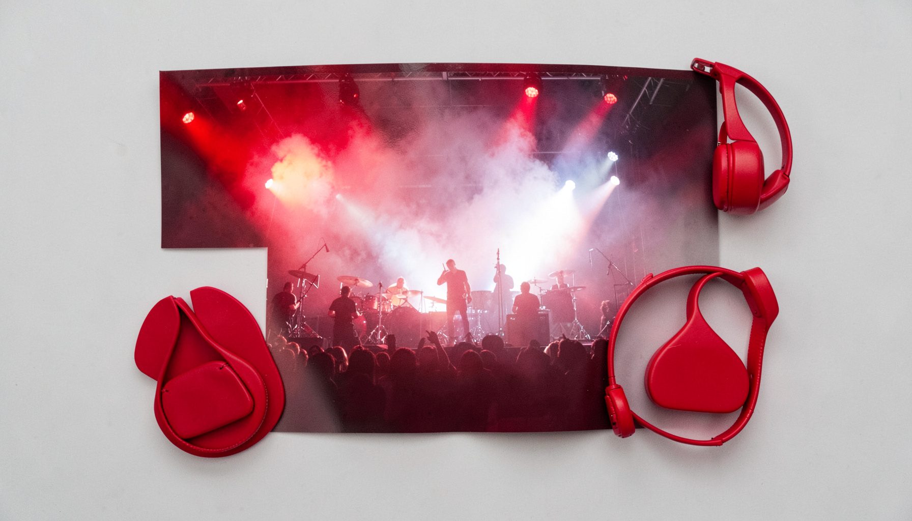 Wide shot of a live performance with backlit figures on stage, dense fog illuminated by crimson and white spotlights