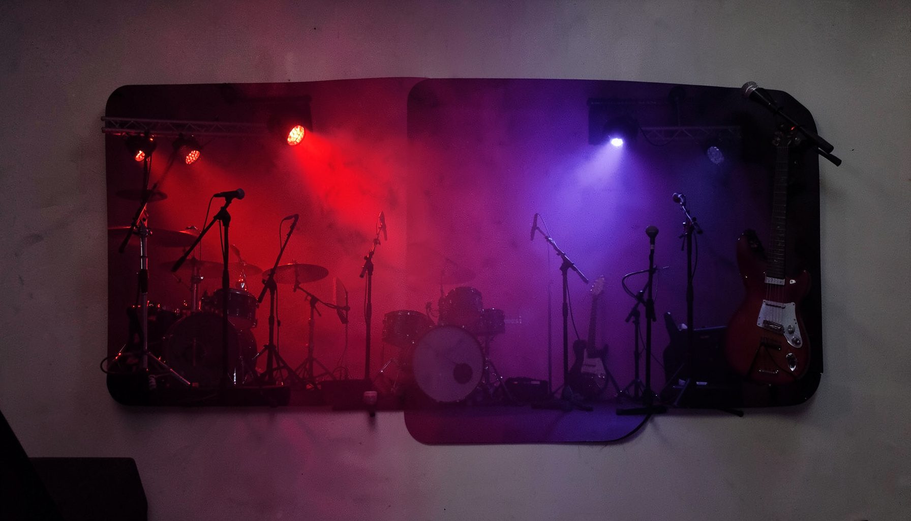 Dark concert-stage scene with deep red and blue stage lighting cutting through haze, silhouetted instruments and microphones